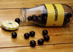 round chocolates falling on wooden table with bottle's cap opened