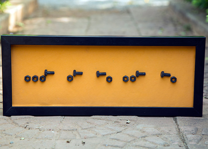 Black rectangle with morse code name formed with nuts and bolts