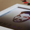 close up of logo edited face in a white one inch frame with banner in the background